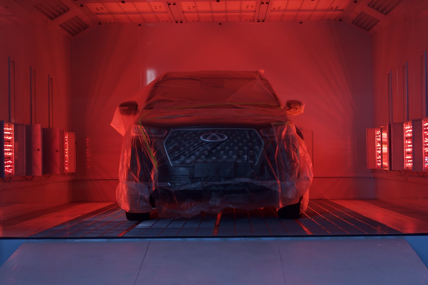 A vehicle inside a red-lit automotive paint booth