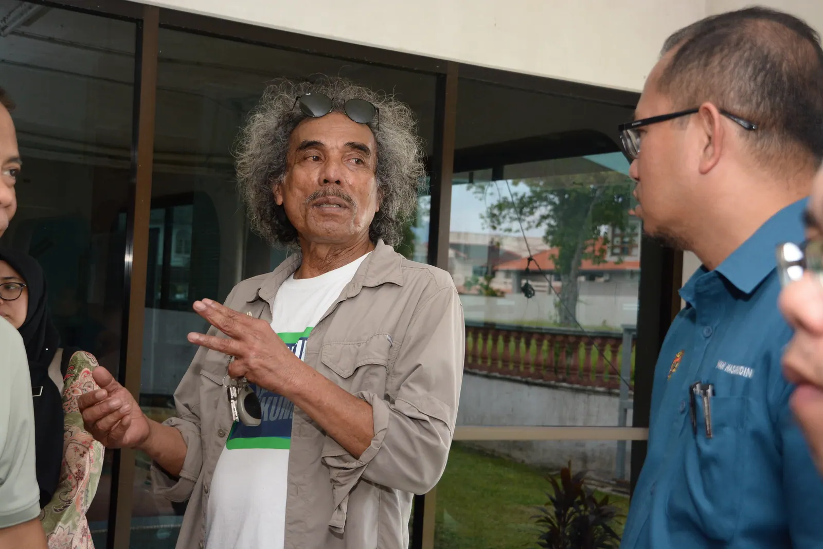 An older man speaking with an expressive hand gesture during a community visit